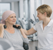 junge Frau mit Kopfbedeckung wird von einer Trainerin an einem Trainingsgerät angeleitet