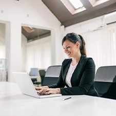 Junge Frau schreibt auf ihrem Notebook und sitzt in einem großen, hellen Raum
